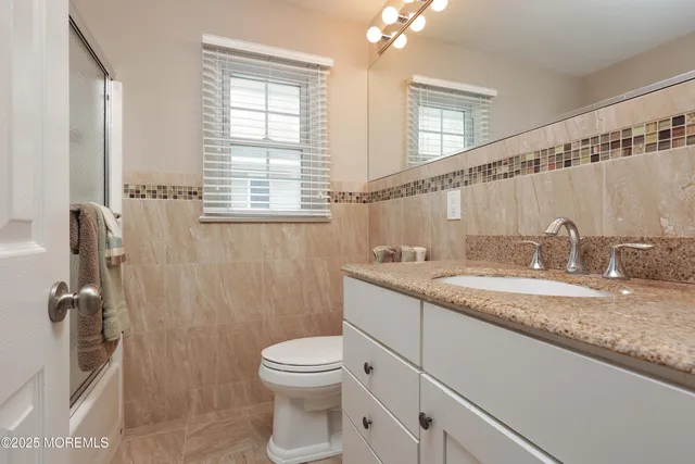 a bathroom with a granite countertop sink a toilet a mirror and shower