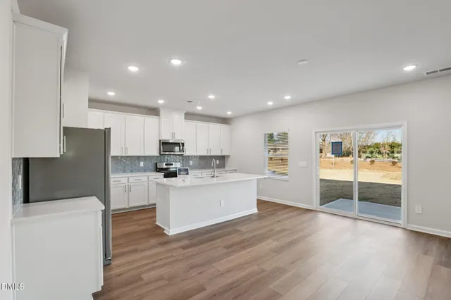 a large kitchen with stainless steel appliances kitchen island a refrigerator a sink dishwasher a stove and white cabinets with wooden floor