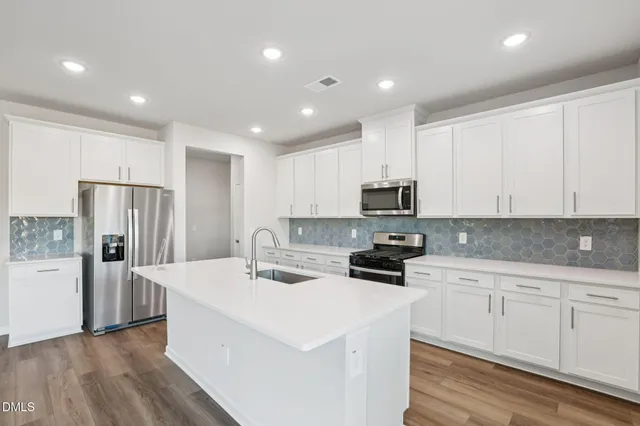 a large kitchen with kitchen island a sink a stove a refrigerator and white cabinets with wooden floor