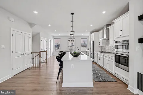 a kitchen with stainless steel appliances kitchen island granite countertop a stove a sink a refrigerator and white cabinets with wooden floor