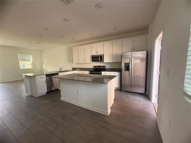 a kitchen with stainless steel appliances granite countertop a stove a sink dishwasher a refrigerator and white cabinets with wooden floor