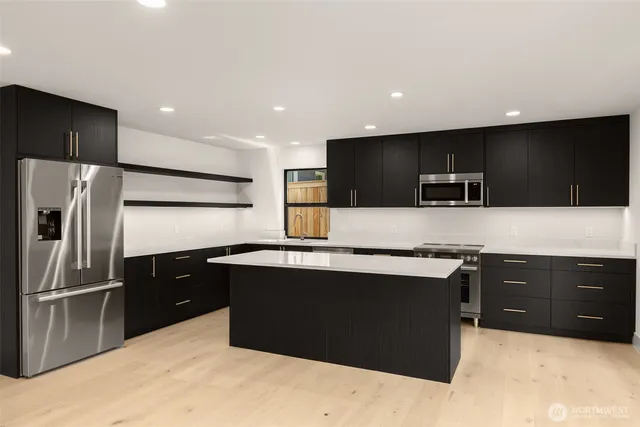 a large kitchen with stainless steel appliances kitchen island granite countertop a refrigerator oven a sink with a countertops and wooden floor