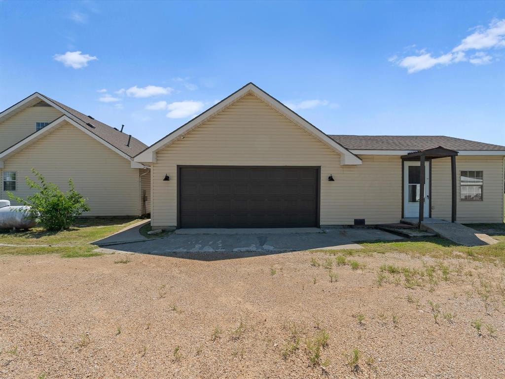 289 County Road 4655 Rhome, TX 76078 - Photo 22 of 34 Light-colored siding exterior featuring an attached garage with a dark sectional door, a covered entry with a screen door to the ADU