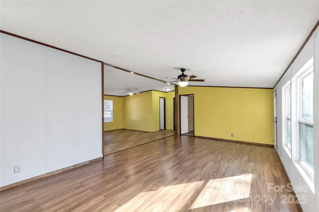 an empty room with wooden floor chandelier fan and windows
