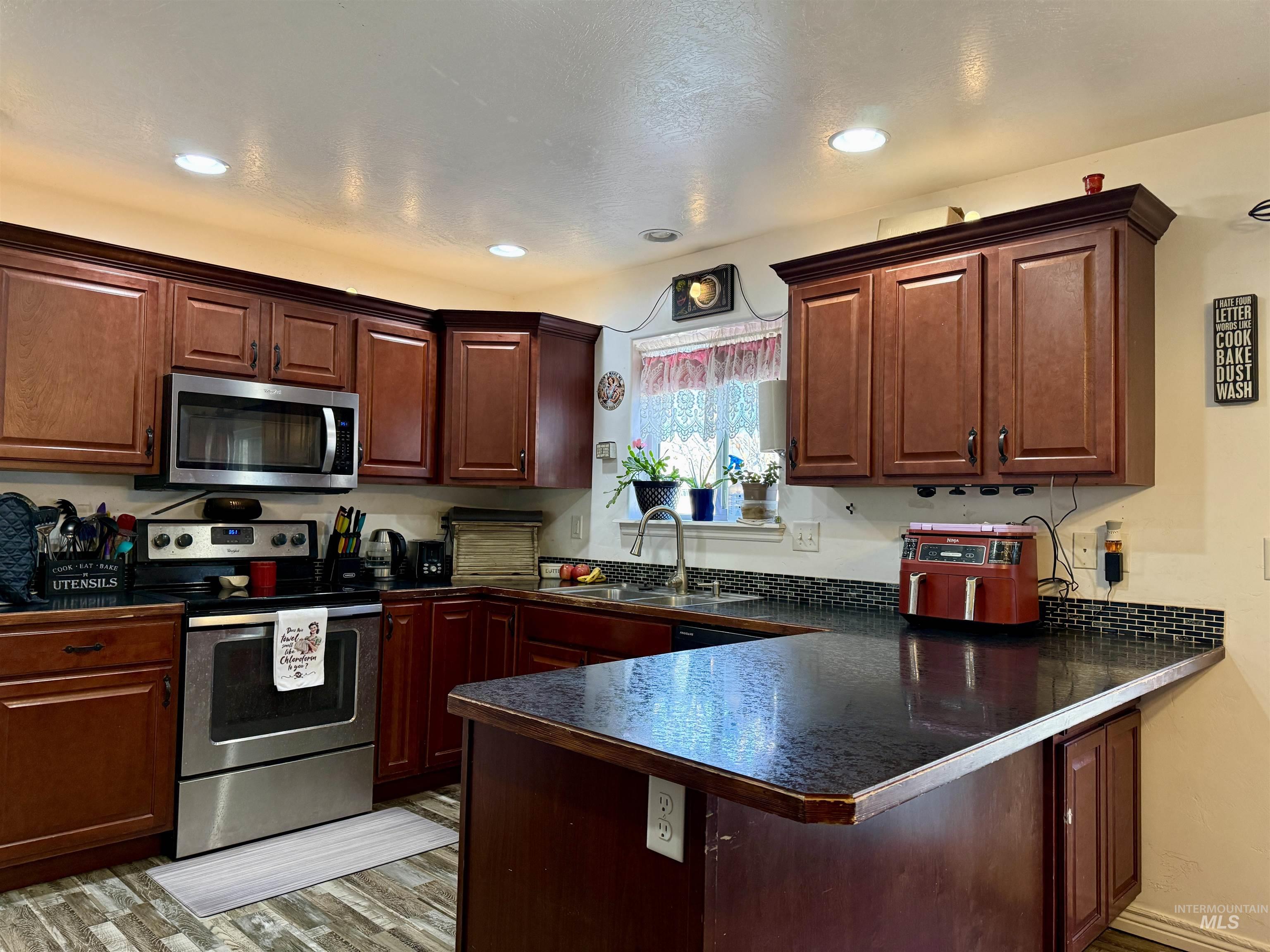 1141 Sunset Lane Kimberly, ID 83341 - Photo 2 of 6 Kitchen featuring stainless steel appliances, dark countertops, a peninsula, light wood-style floors, and dark wood finish cabinets