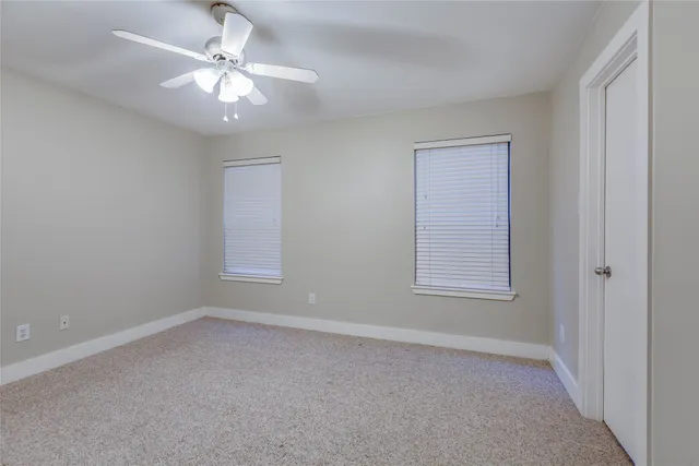 an empty room with a chandelier fan and windows
