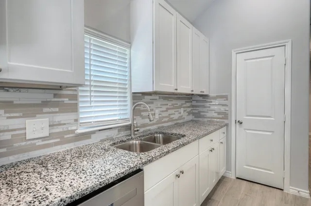 a kitchen with granite countertop a sink and white cabinets