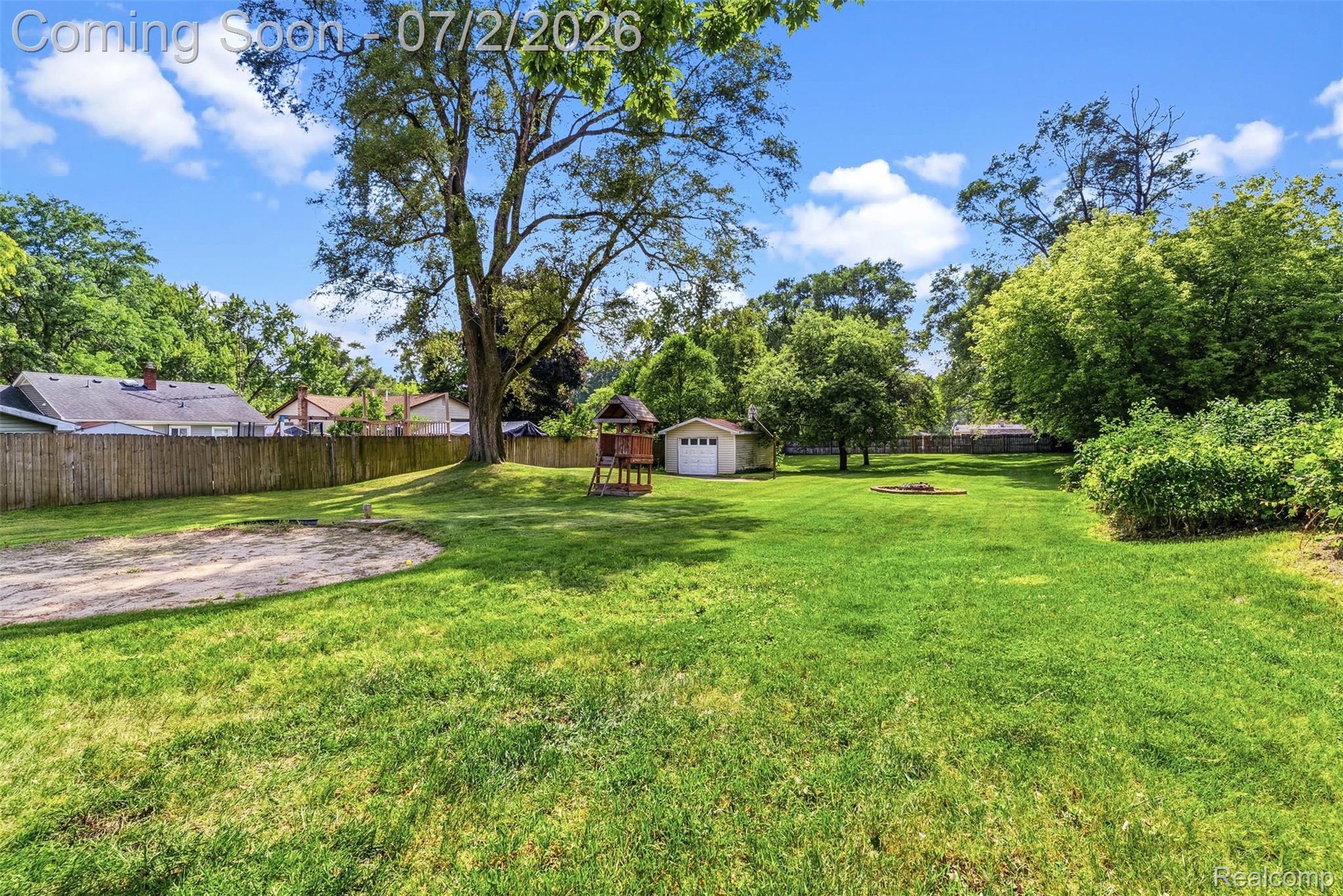 305 East Road Holly, MI 48442 - Photo 30 of 41 Expansive backyard featuring a lush lawn, mature trees, wood privacy fencing, and a detached white storage shed with a roll-up garage door