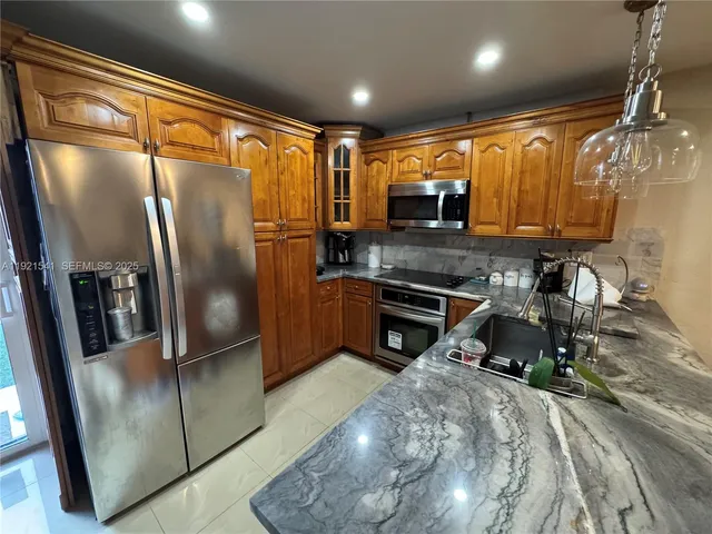 a kitchen with stainless steel appliances granite countertop a refrigerator a stove and a sink with wooden floor
