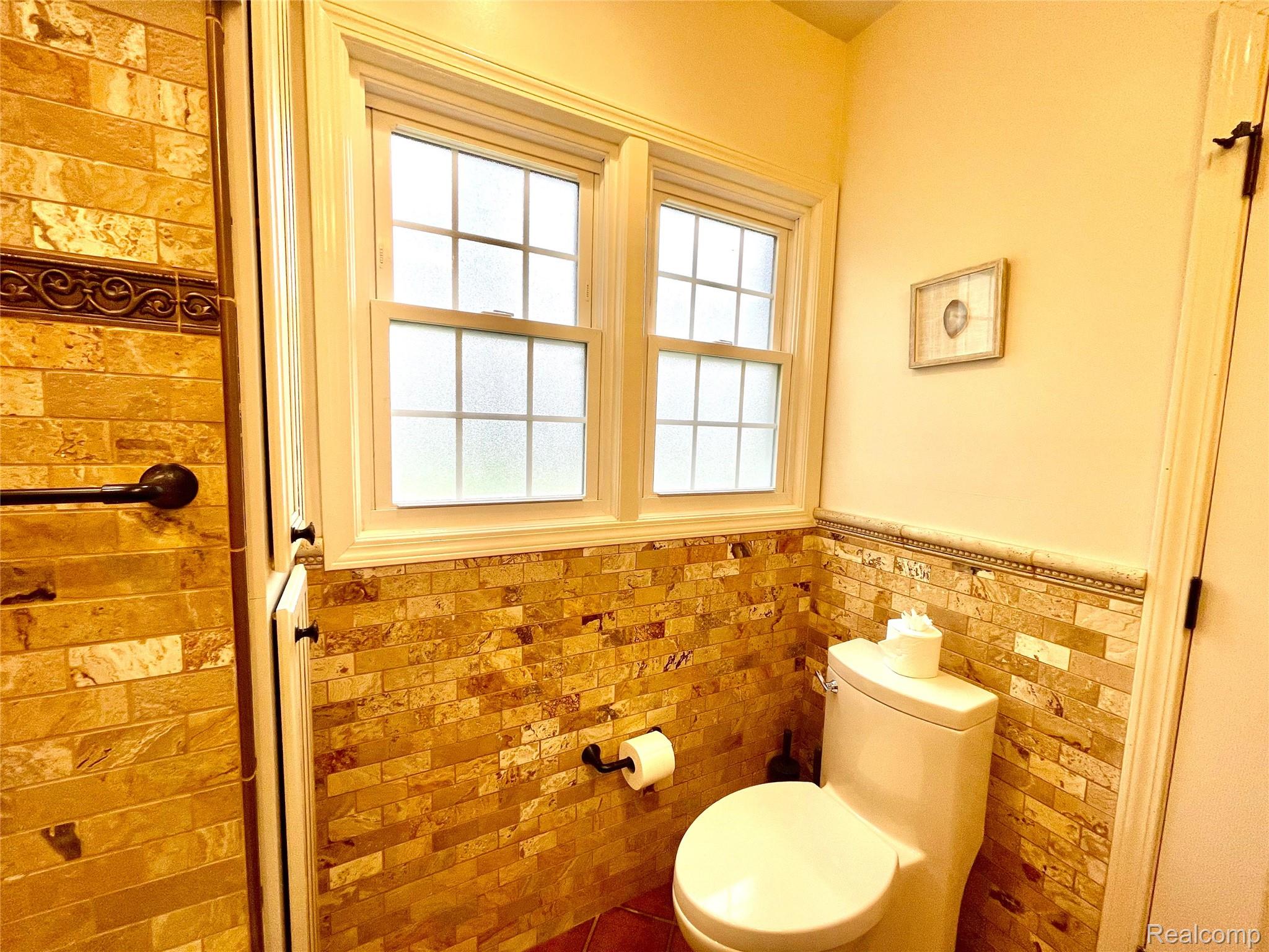 60 Devon Road Bloomfield Hills, MI 48302 - Photo 29 of 50 Bathroom featuring full-height stone tile walls, a dual-pane window with privacy glass, crown molding, and a built-in toilet paper holder