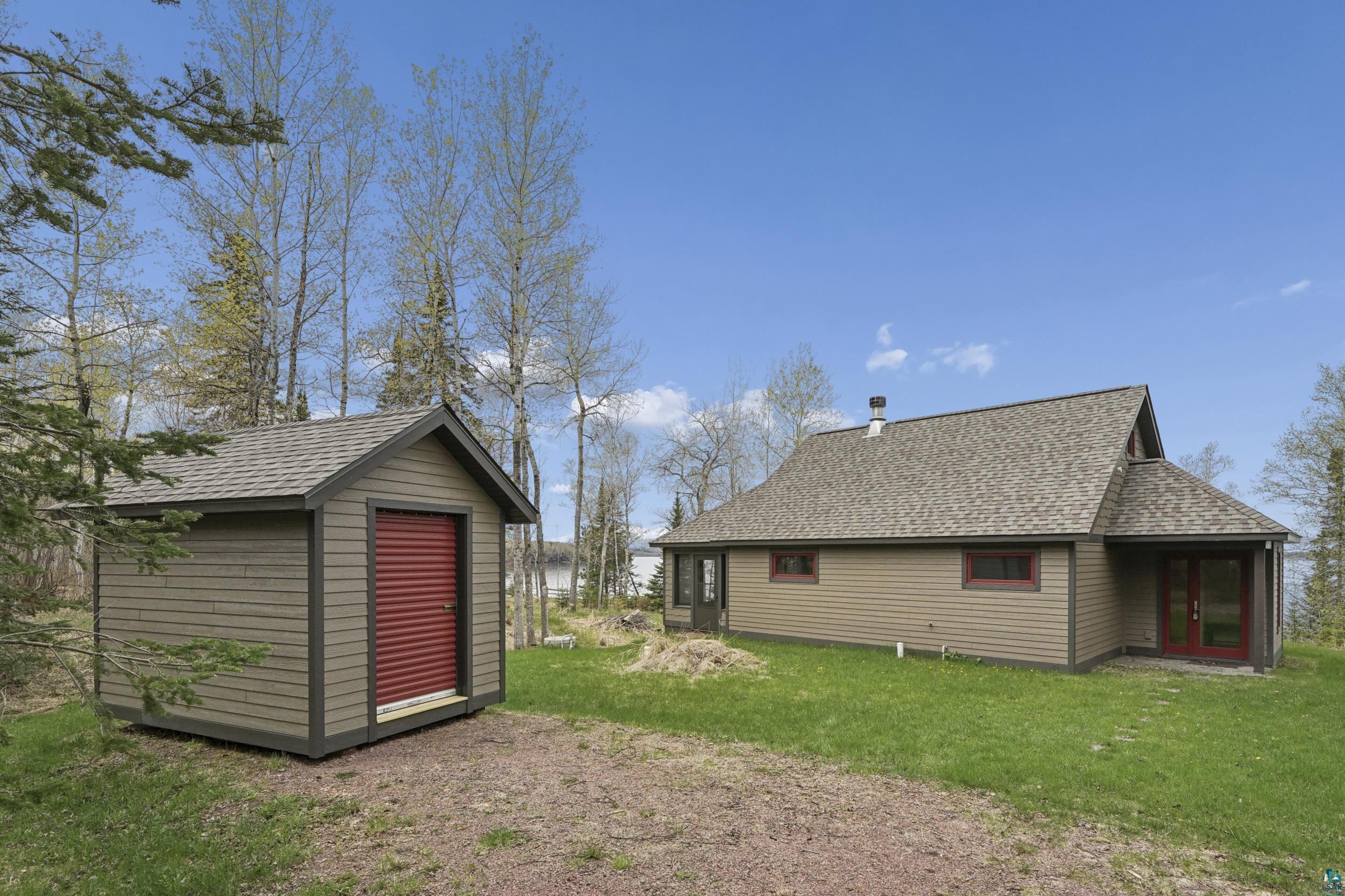 89095 West Romans Point Road Herbster, WI 54844 - Photo 8 of 30 Exterior of a single-story residence featuring tan horizontal siding, a gray shingle roof, and red trim accents