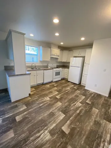 a open kitchen with kitchen island a sink dishwasher stove with white cabinets and wooden floor