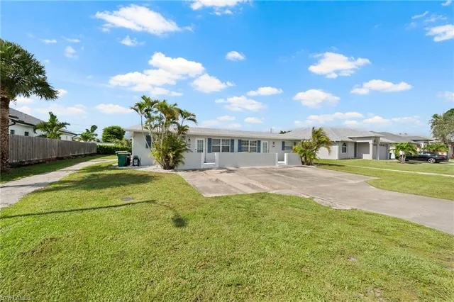 a view of yellow house with a big yard and potted plants