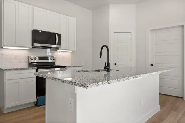 a kitchen with stainless steel appliances granite countertop a sink a microwave a stove and white cabinets with wooden floor