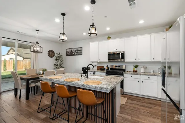 a kitchen with stainless steel appliances granite countertop a stove top oven a refrigerator a sink and a dining table with white cabinets