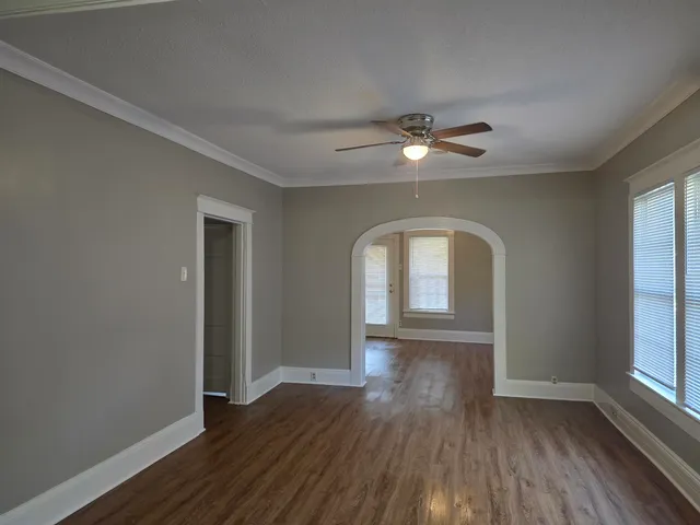 an empty room with wooden floor chandelier fan and windows