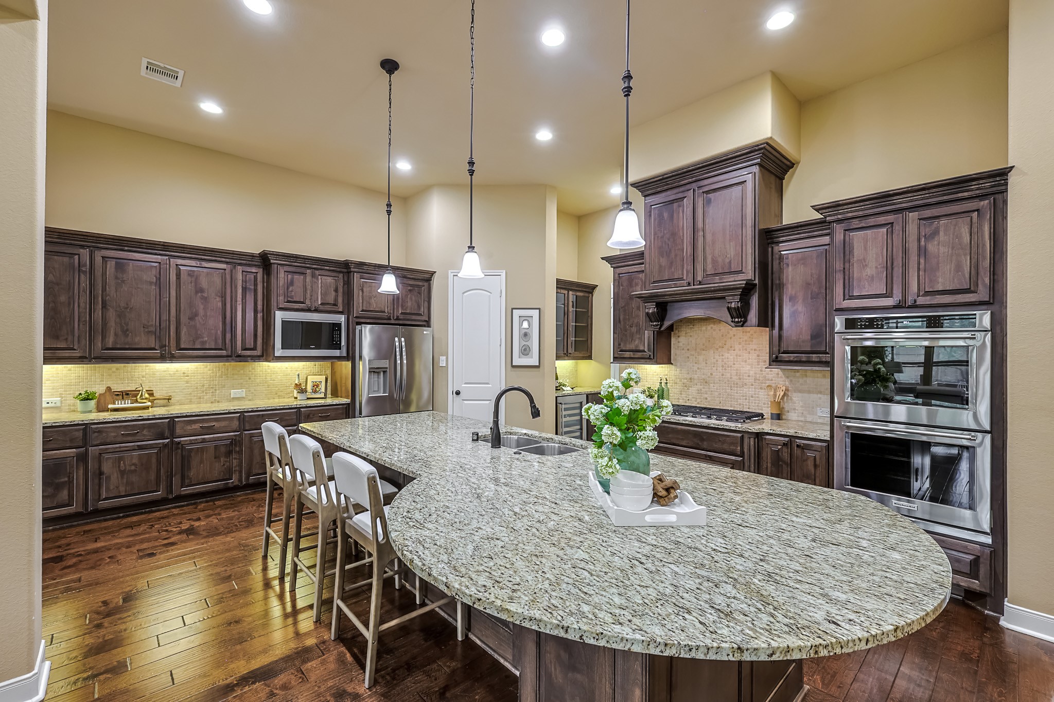 515 Mill Creek Road Pinehurst, TX 77362 - Photo 16 of 48 This kitchen features elegant dark wood cabinetry, a large granite island with seating, stainless steel appliances, and pendant lighting, offering a spacious and inviting cooking and gathering area.