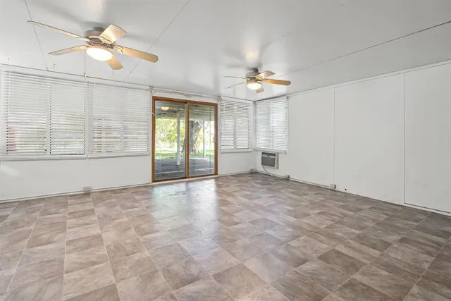 an empty room with chandelier fan and windows