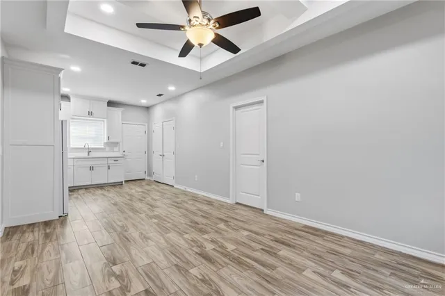 a view of an empty room and kitchen view with wooden floor