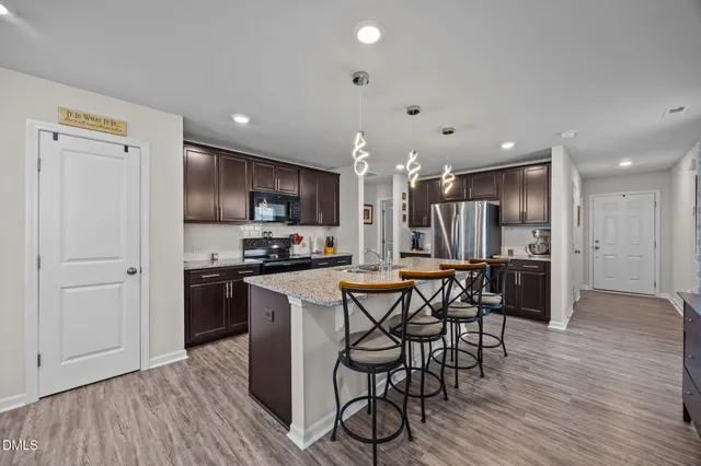 a kitchen with stainless steel appliances kitchen island granite countertop a refrigerator a stove a sink a dining table and chairs with wooden floor
