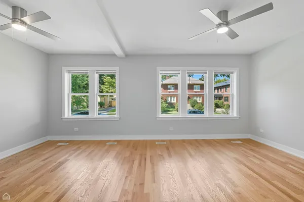 an empty room with wooden floor ceiling fan and windows