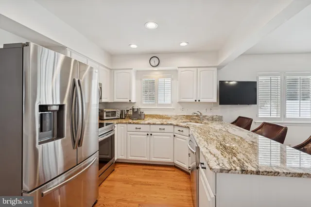 a kitchen with stainless steel appliances granite countertop a refrigerator a stove a microwave oven a sink dishwasher and white cabinets with wooden floor
