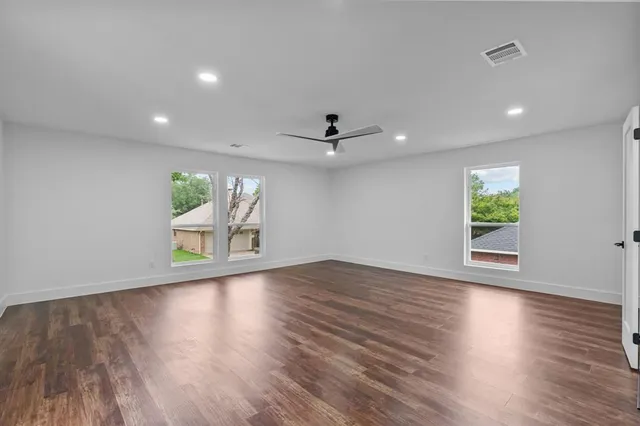 an empty room with wooden floor a ceiling fan and windows