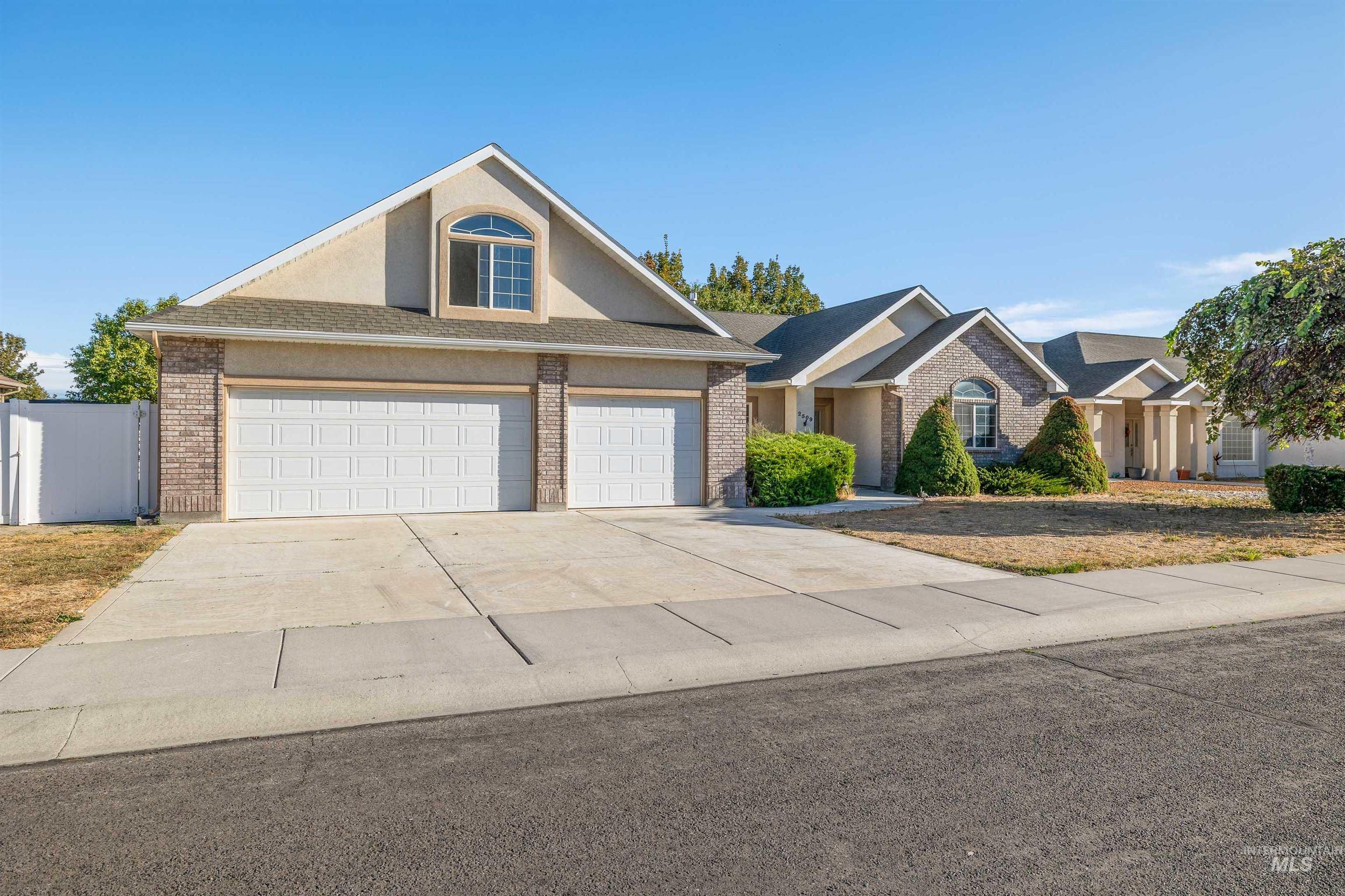 2509 Cedar Ridge Road Twin Falls, ID 83301 - Photo 29 of 36 Three-car garage with panel doors, brick and stucco exterior, arched window, concrete driveway, and established landscaping