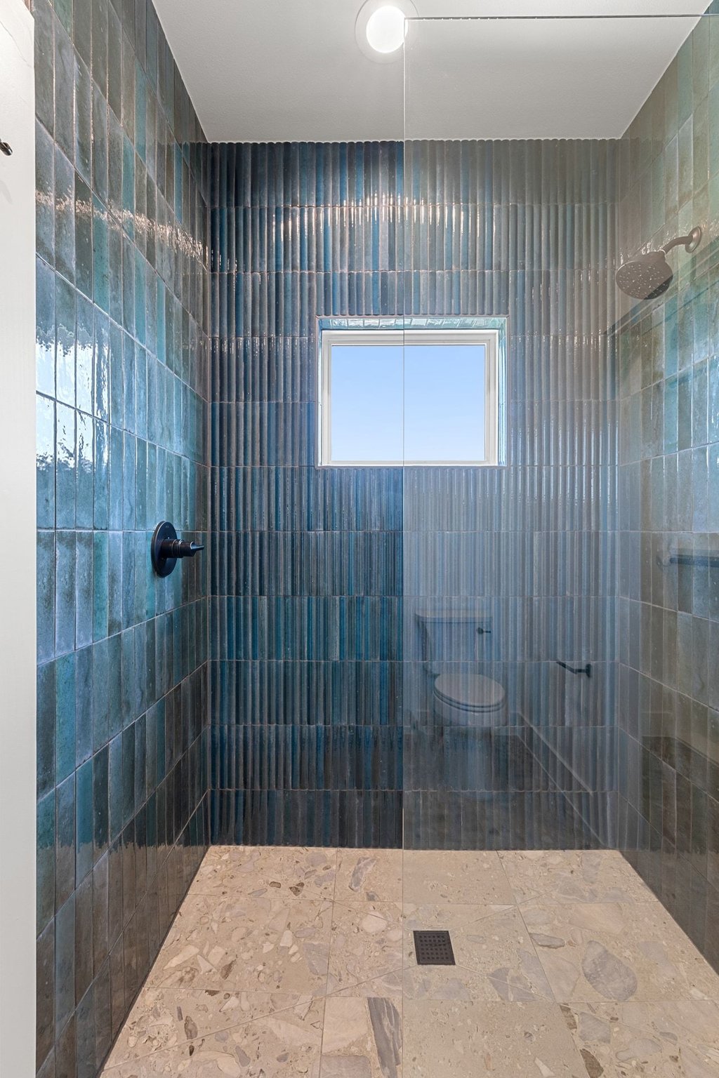 9207 Zyle Road Austin, TX 78737 - Photo 30 of 40 A striking walk-in shower features rich blue tile walls and a light-toned stone floor, illuminated by a high window.