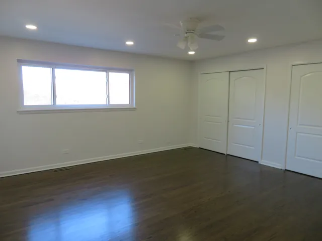 an empty room with wooden floor and windows with curtains