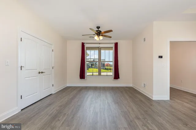 an empty room with wooden floor chandelier fan and windows