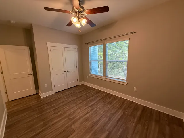 an empty room with wooden floor fan and windows