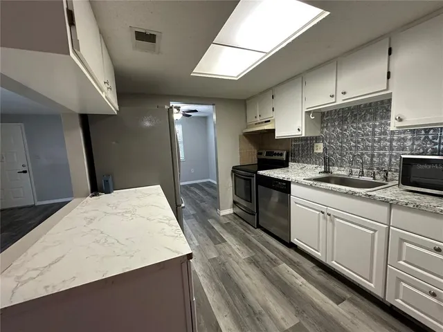 a kitchen with granite countertop a sink stainless steel appliances wooden floor and cabinets