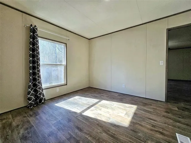 an empty room with wooden floor and windows with curtains