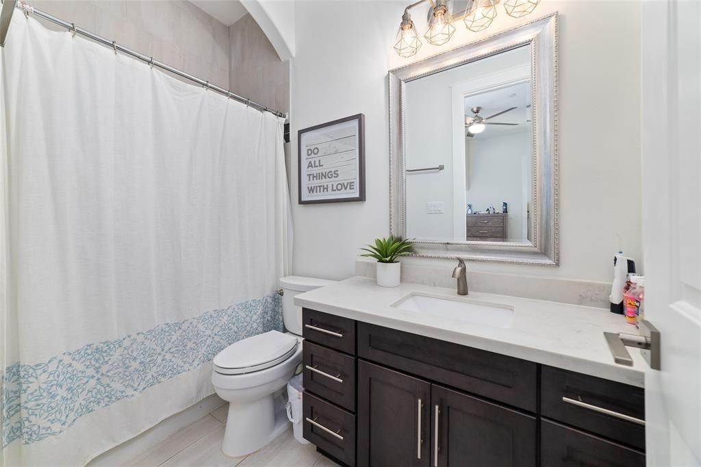 710 Delano Street, Unit A Houston, TX 77003 - Photo 19 of 32 This bathroom features a modern design with a dark wood vanity, a white countertop, and a sleek sink. It includes a large framed mirror with stylish lighting above and light flooring.
