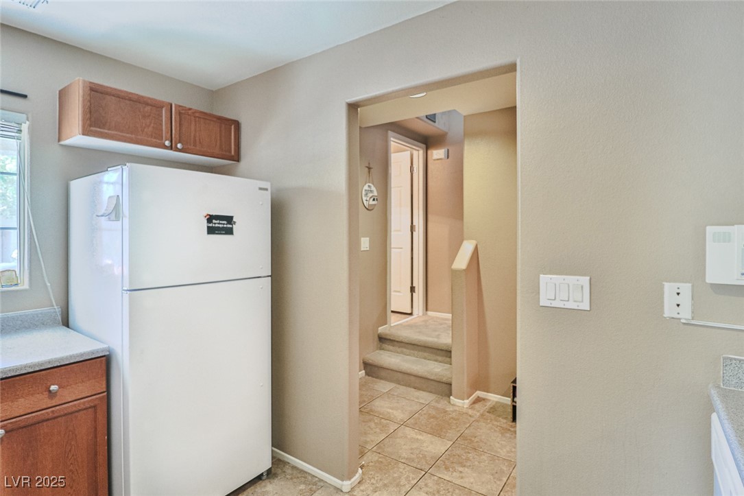 9068 West Alluring Avenue Las Vegas, NV 89149 - Photo 11 of 48 Kitchen with freestanding refrigerator, brown cabinets, light tile patterned flooring, and light countertops