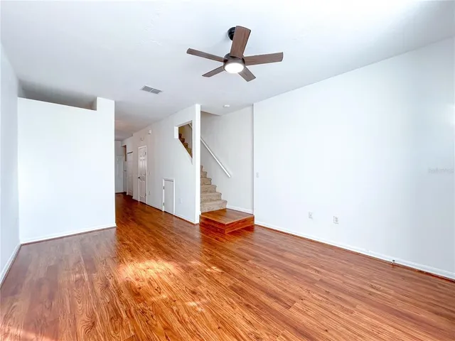 a view of an empty room with wooden floor and a ceiling fan