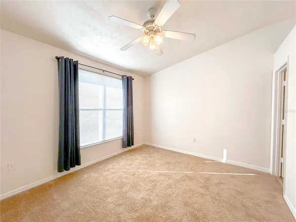 an empty room with chandelier fan and windows
