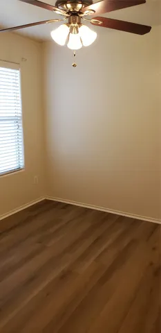 an empty room with wooden floor fan and windows