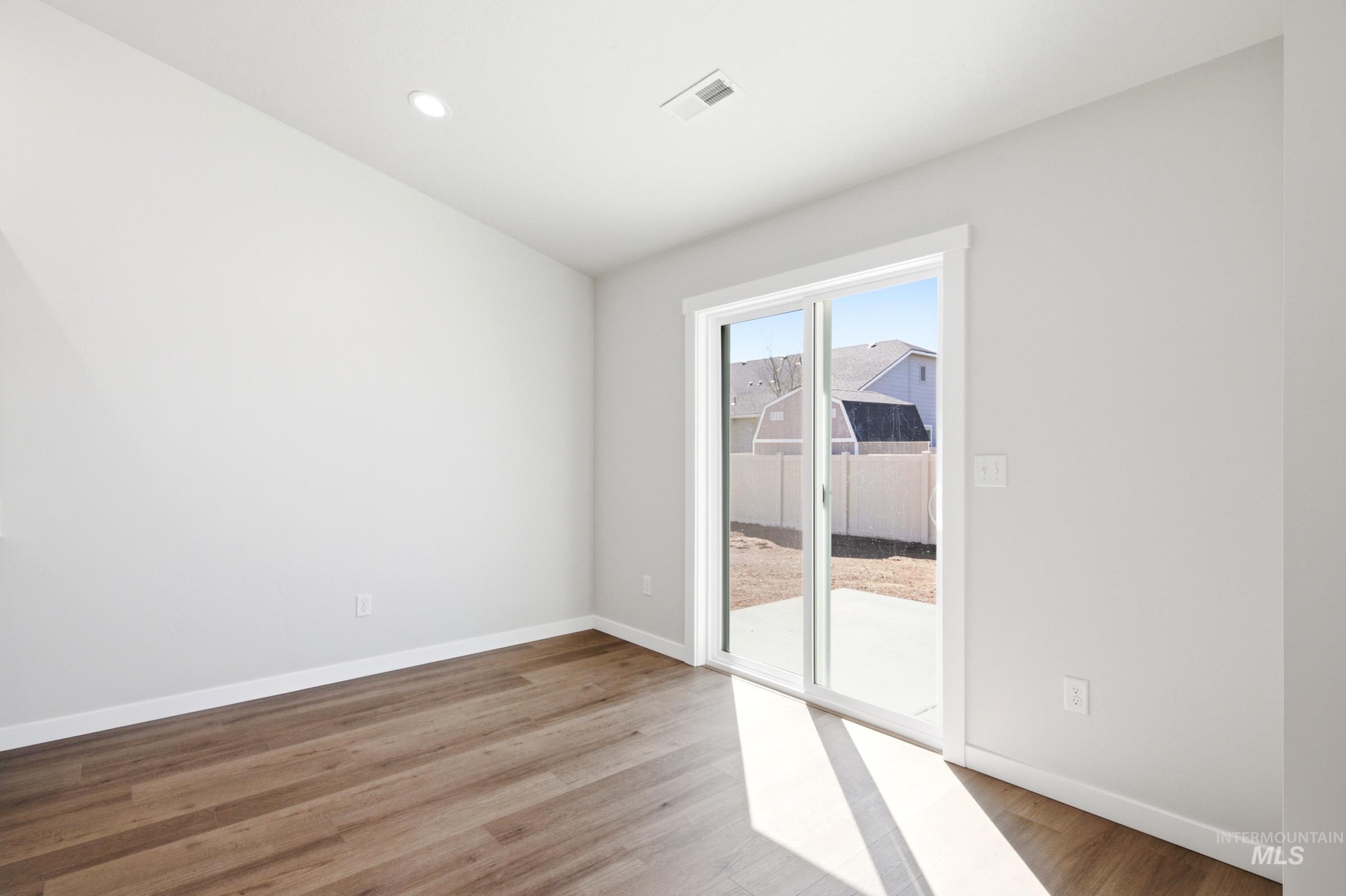 12877 Decatur Street Nampa, ID 83651 - Photo 9 of 22 Spacious room featuring wood-finish flooring, light-toned wall paint, recessed lighting, white baseboards, and a glass sliding door opening to an outdoor patio area