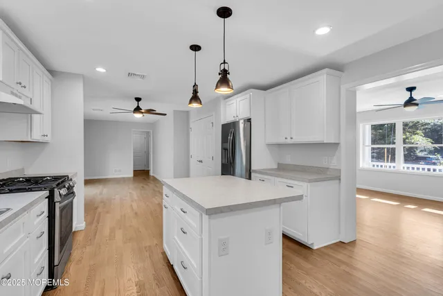 a open kitchen with kitchen island a stove a sink a refrigerator and white cabinets with wooden floor