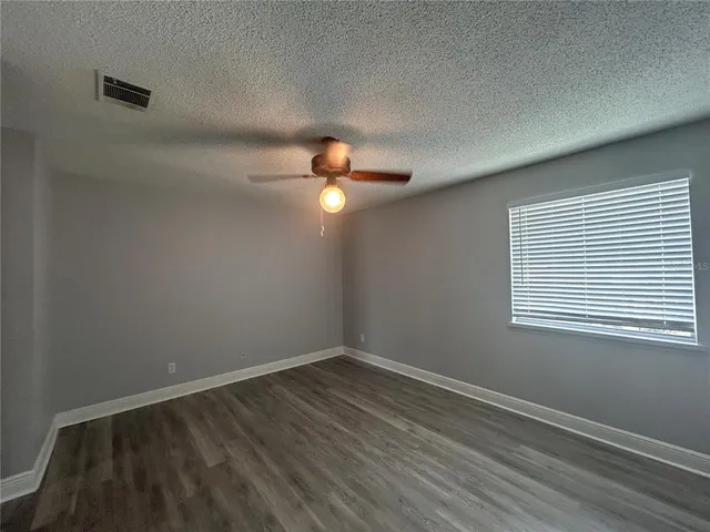 an empty room with wooden floor fan and windows