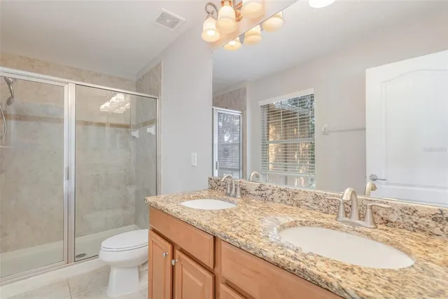 a bathroom with a granite countertop double vanity sink toilet and shower