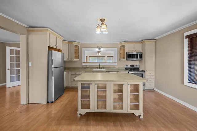 a kitchen with stainless steel appliances kitchen island granite countertop a refrigerator a stove a sink dishwasher and white cabinets with wooden floor