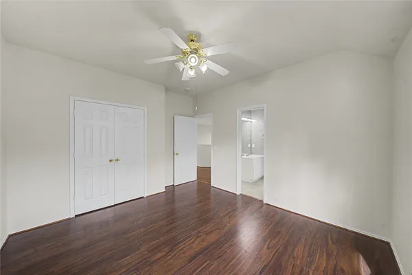 a view of an empty room with wooden floor and a ceiling fan