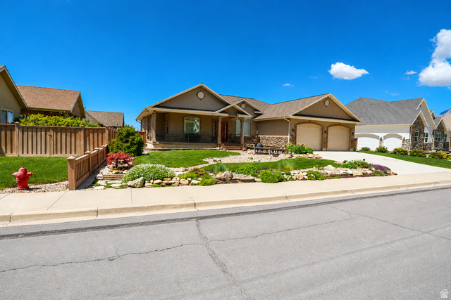1055 North 1000 East Mapleton, UT 84664 - Photo 109 of 112 Stucco and stone exterior featuring a covered front porch, an attached two-car garage, and a landscaped front yard with mature plantings