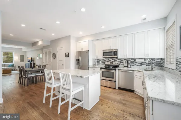 a kitchen with stainless steel appliances granite countertop a stove a sink dishwasher a refrigerator and white cabinets with wooden floor