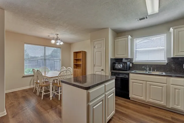 a kitchen with stainless steel appliances granite countertop a stove top oven a sink dishwasher a dining table and chairs with wooden floor