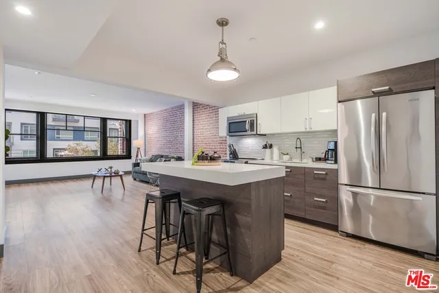 a kitchen with stainless steel appliances granite countertop a refrigerator a sink dishwasher a stove and a dining table with wooden floor