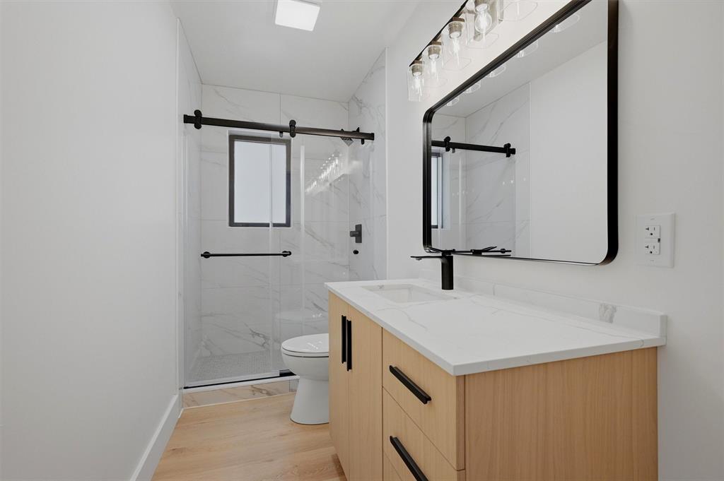 410 Arkansas Road Sadler, TX 76264 - Photo 25 of 40 Contemporary bathroom featuring a light wood-finish vanity with a white countertop, a rectangular black-framed mirror, and a glass-enclosed shower with black hardware